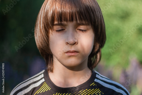 A boy with long hair standing among lupins in the rays of the sun.