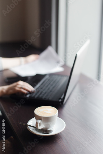 Hands behind the laptop on the background of a cup of coffee