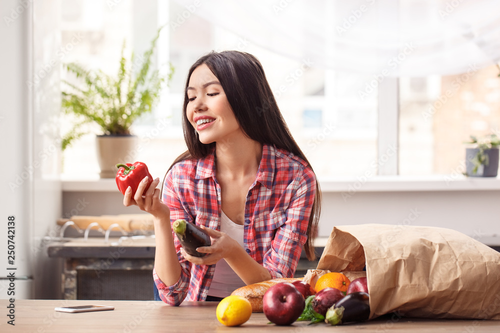 Young girl at kitchen healthy lifestyle standing looking at bell pepper joyful near bag on table