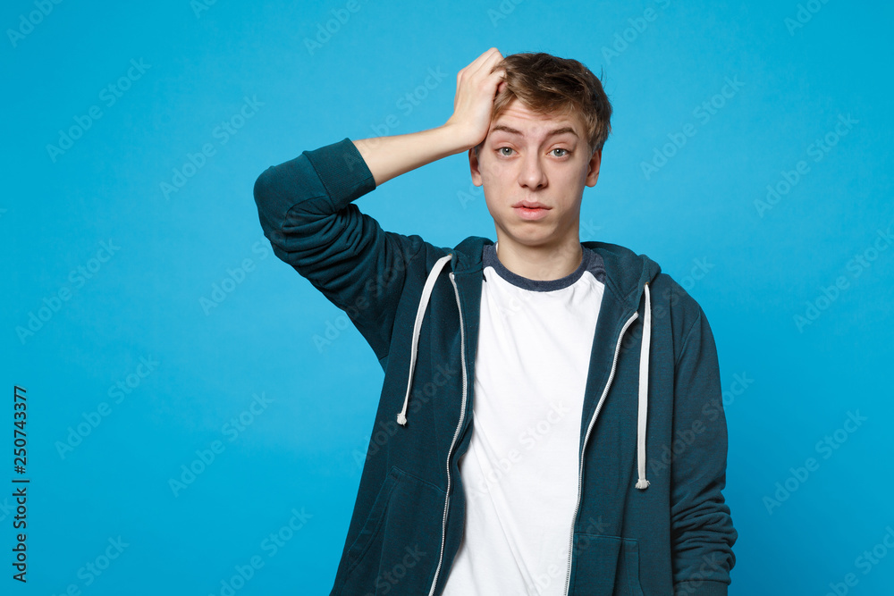 Portrait of perplexed young man in casual clothes putting hand on head isolated on blue wall background in studio. People sincere emotions lifestyle concept. Mock up copy space. Advertising area. Portrait of perplexed young man in casual clothes putting hand on head isolated on blue wall background in studio. People sincere emotions lifestyle concept. Mock up copy space. Advertising area.