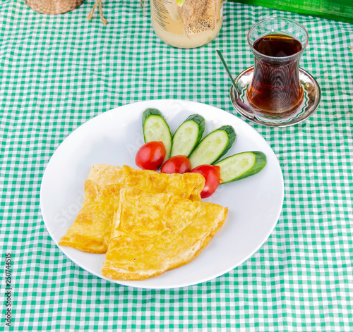 Omelette, cucumber, tomato and turkish tea on a green checkered tablecloth. Turkish breakfast