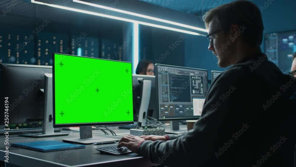 Smart Male IT Programer Working on Desktop Green Mock-up Screen Computer in Data Center System Control Room. Team of Young Professionals Programming Sophisticated Code