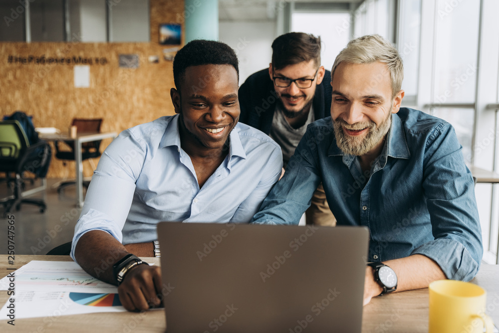 Business colleagues. Young successful smiling colleagues are looking into a laptop in their creative office Business colleagues. Young successful smiling colleagues are looking into a laptop in their creative office