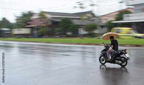 Yala  Thailand  November  19  2018  Motion Blurred panning photo of man riding motorcycle in the rain on road and holding umbrella raining season