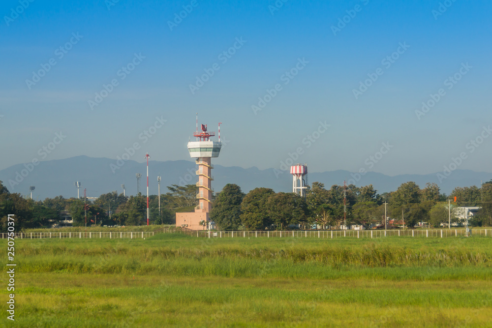 Airplane control tower on the green grass field with blue sky background at Chiang Rai International Airport, Thailand.
