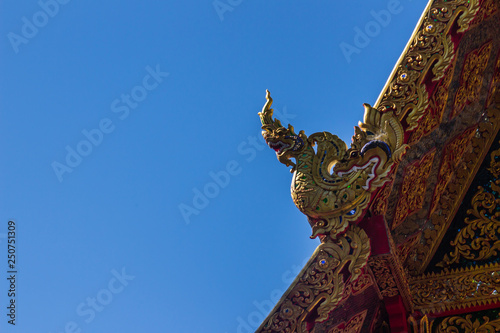 Beautiful golden naga sculptures on the church roof under the blue sky background at Wat Phra That Doi Tung, one of which is believed to contain the left collarbone of Lord Buddha. © kampwit
