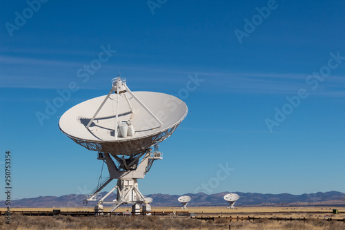 Very Large Array radio antenna dish close with others in distance, blue sky copy space, horizontal aspect