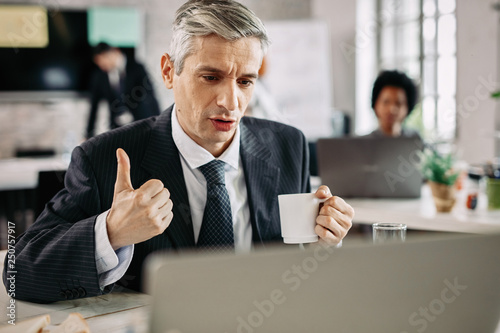 Businessman showing thumb up while working on the computer.