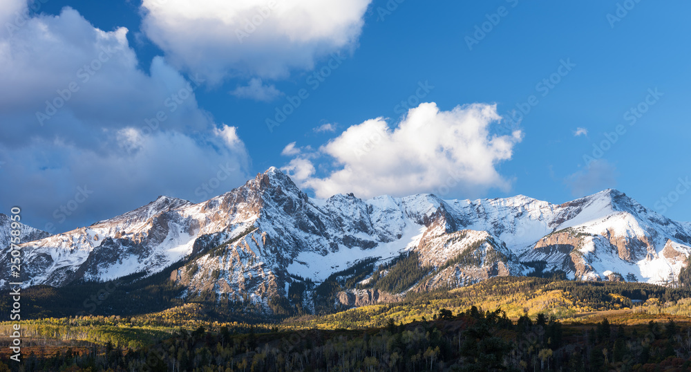 Mount Sneffels is within the Uncompahgre National Forest. An early fall snowstorm covers the mountain range  with aspen groves in full colo