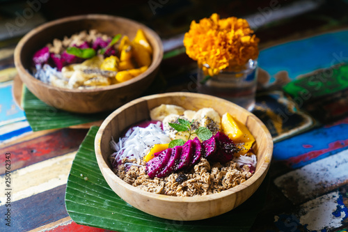 Close up four smoothie bowls made with mango  banana  granola  grated coconut  dragon fruit  chia seeds and mint on colored background