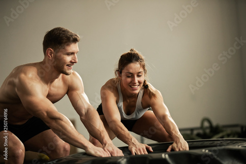 Happy athletic couple exercising with large tire at cross training.