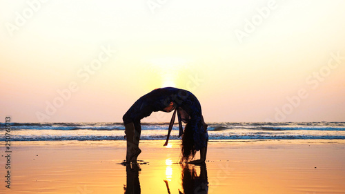 Silhouette of young sporty woman doing gymnastic bridge on the beach at beautiful sunset