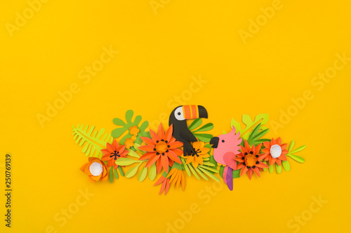 Decorative composition of tropical leaves and flowers. Yellow background. Toucan bird and pink parrot. Paper craft.