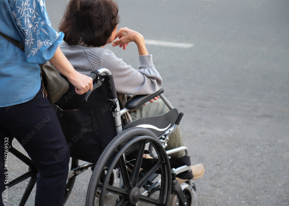 Closeup of elderly disabled Asian woman in wheelchair assists by female assistant. Symbol of ageing society. Closeup of elderly disabled Asian woman in wheelchair assists by female assistant. Symbol of ageing society.