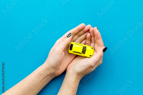 Car insurance concept. Safety of auto. Car toy in female hands on blue background top view copy space