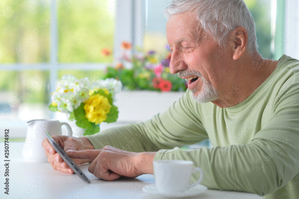 Close up portrait of senior man using tablet while drinking tea Close up portrait of senior man using tablet while drinking tea