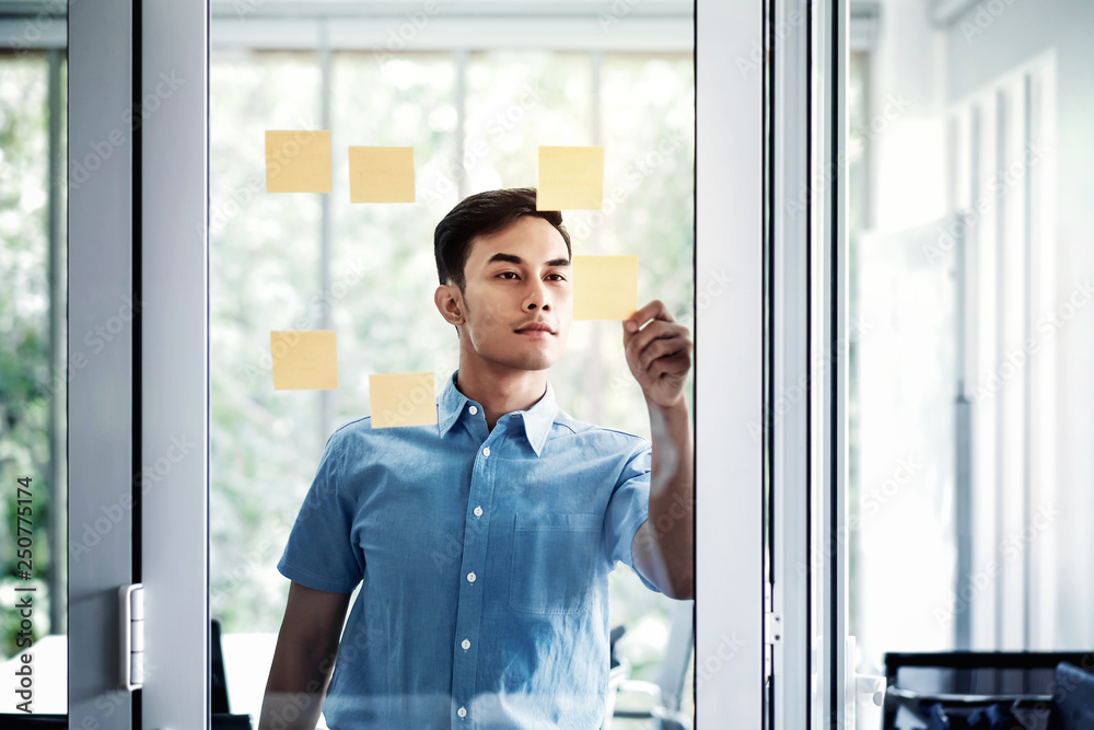 Fototapeta premium Young Asian Businessman Working in Office Meeting Room. Man Analyzing Data Plans and Project. Concentrate on Document Note on Board