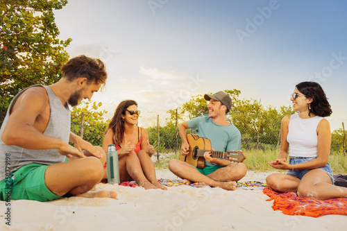 Lifestyle beach of group of young friends playing guitar and enjoying