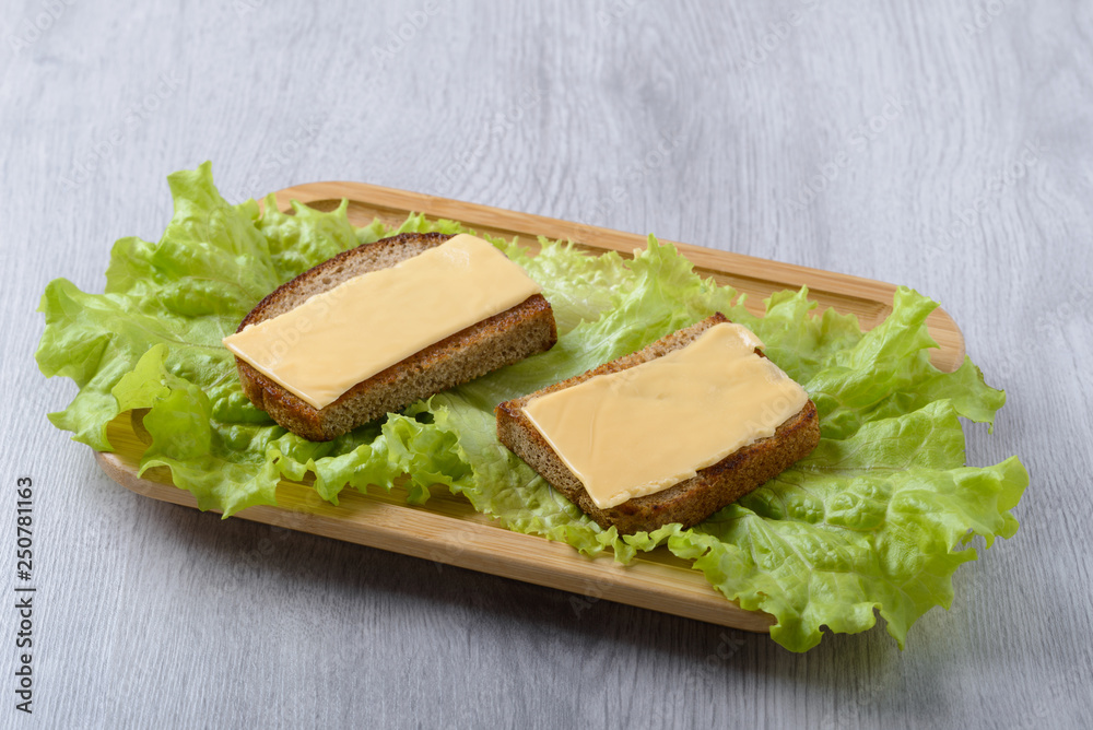 toast with lettuce leaf and cheese on a wooden plate