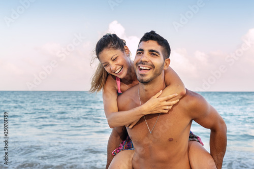 Lifestyle portrait of young couple piggyback ride at the beach © Guajillo studio