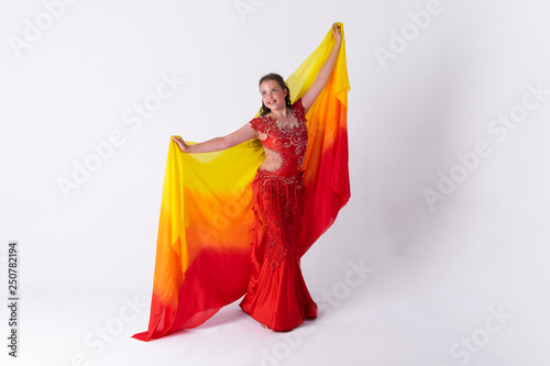 Young girl with shawl and in red dress performs oriental dance on white background