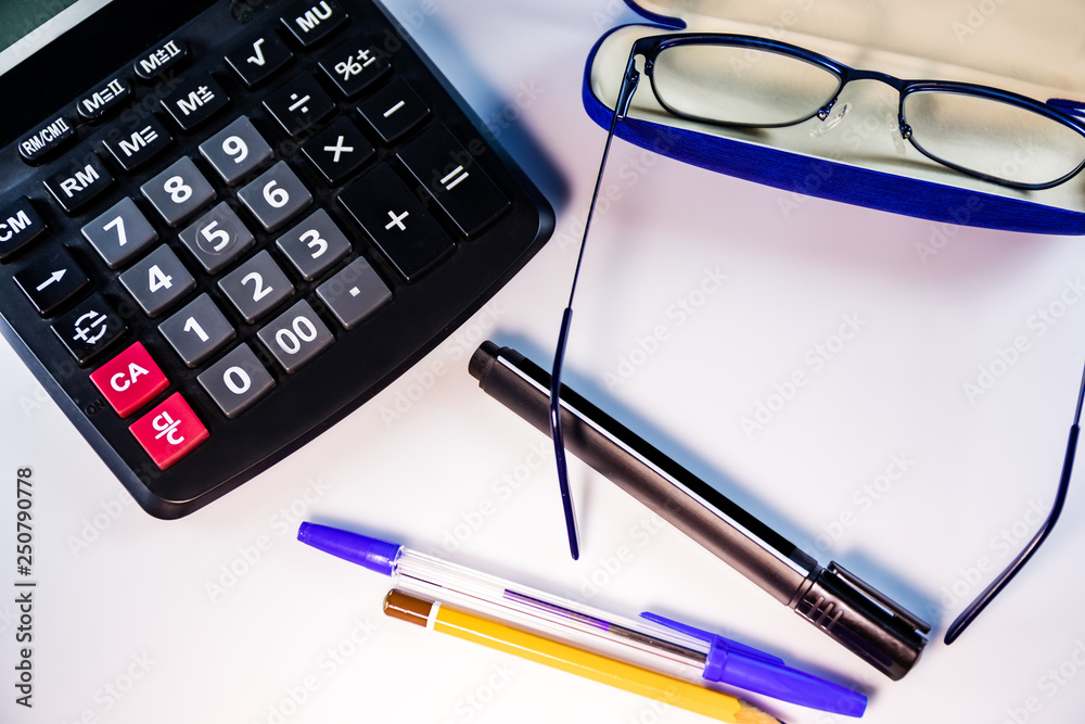 Calculator, glasses, pens and pencil on white table. Workplace office worker. Calculator, glasses, pens and pencil on white table. Workplace office worker.