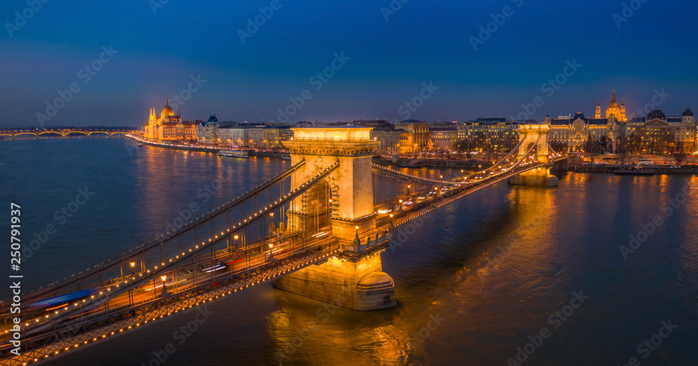 Fototapeta premium Budapest, Hungary - Aerial panormaic view of the famous illuminated Szechenyi Chain Bridge at blue hour with Parliament building and St.Stephen's Basilica at the background