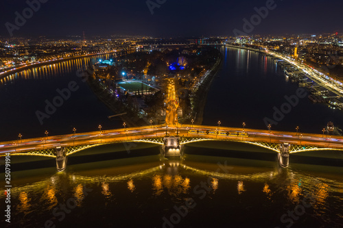 Budapest, Hungary - Aerial view of the illuminated Margaret Bridge with yellow tram on it and Margaret Island at background by night