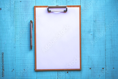 Clipboard with white sheet on wood background. Top view.Vintage style.