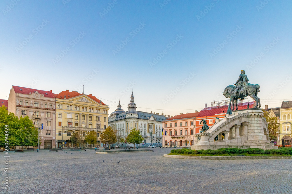 Cluj-Napoca city center. View from the Unirii Square to the Rhedey Palace, Matthias Corvinus Monument and New York Hotel at sunrise on a beautiful, clear sky day
