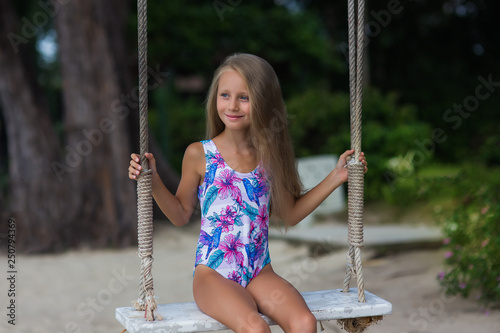 Cute girl with long hair in a swimsuit on a swing on the beach. vacation concept. photo