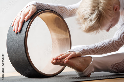 Portrait of gorgeous young woman practicing yoga indoor with a help of yoga wheel. photo