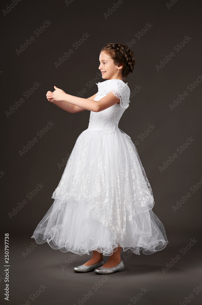 Fototapeta premium little girl is dressed in a white ball gown, dark background