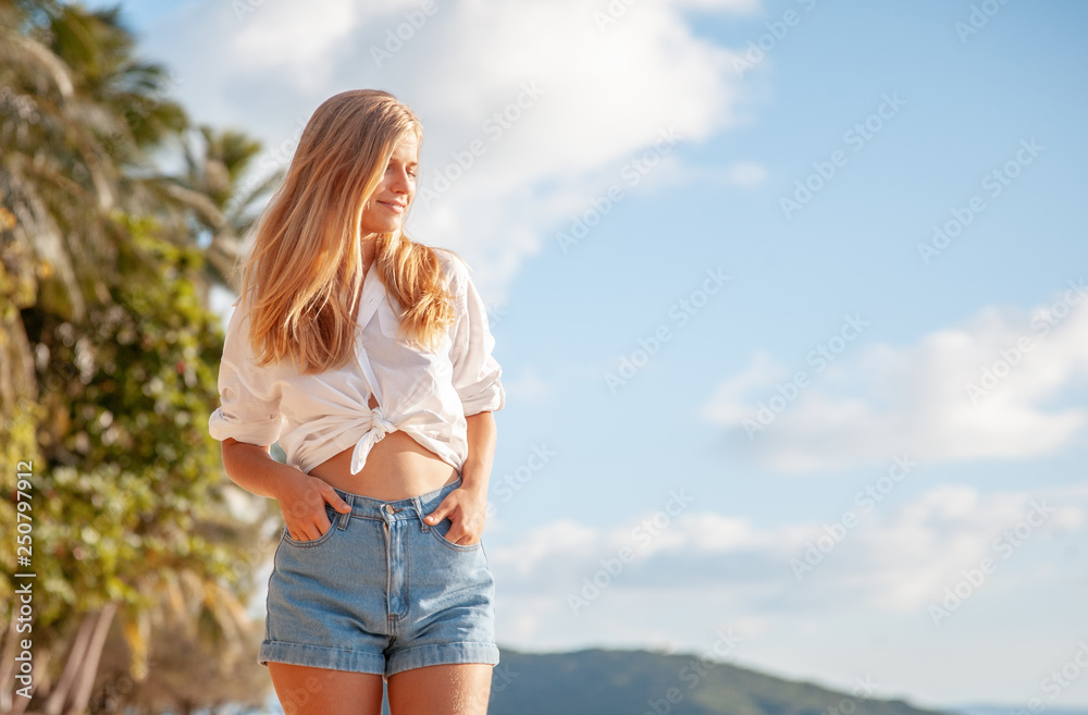 Beautiful young blonde girl with flowing hair and dimples against the blue sky and the sun Beautiful young blonde girl with flowing hair and dimples against the blue sky and the sun