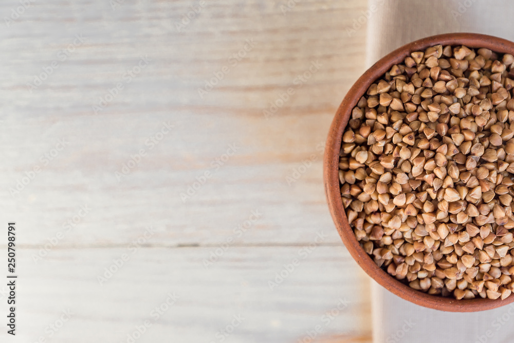 Dry buckwheat in brown clay bowl on wooden table. gluten free grain for healthy diet
