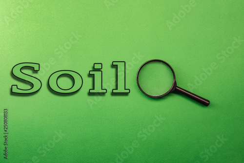 the word SOIL on a green background magnifying glass lying next to search