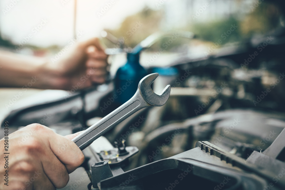 Asian car mechanic holds a wrench and a bottle of lure oil, ready to repair the car. Asian car mechanic holds a wrench and a bottle of lure oil, ready to repair the car.