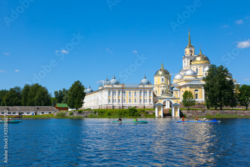 SELIGER, RUSSIA. Nilov Monastery on Seliger lake. Yellow building. Blue sky and blue lake in summer. Kayak people in the foreground