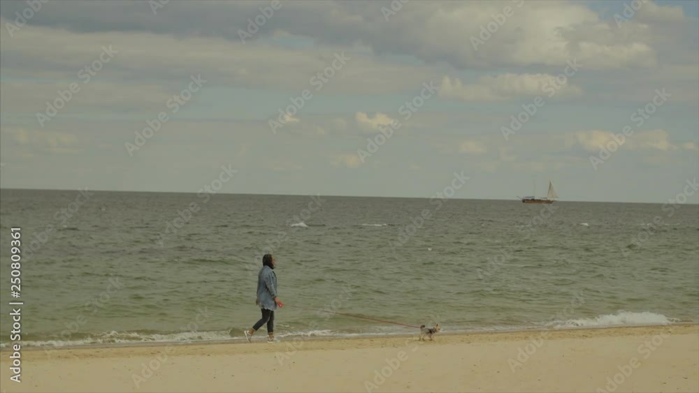 Woman walks with cute dog along the near the sea. Shot from side Woman walks with cute dog along the near the sea. Shot from side