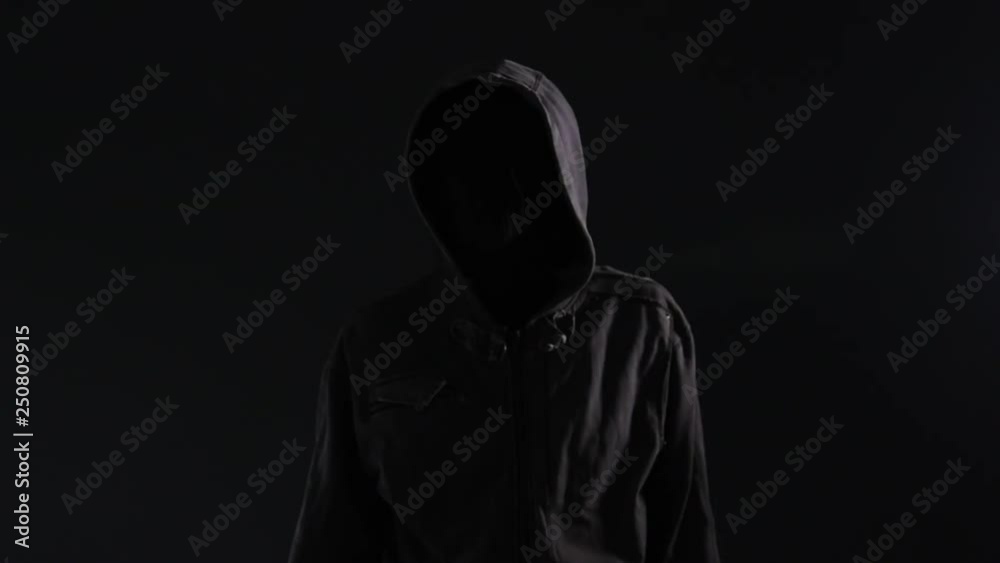 Unrecognizable hooded criminal gesturing finger on lips or shh sign to silence the victim of his crime act, lit by blue and red police light Unrecognizable hooded criminal gesturing finger on lips or shh sign to silence the victim of his crime act, lit by blue and red police light