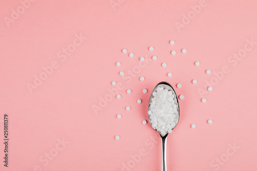 Sugar-replacing tablets with a spoon on a pink background