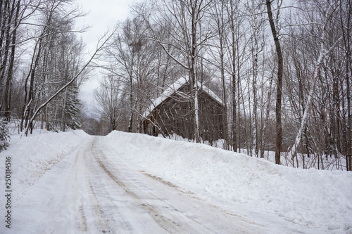 Old barn besides a freshly plowed road in a forested winter landscape. Photographed on Freeman Ridge Road in Kingfield Maine on February 21, 2019. photo