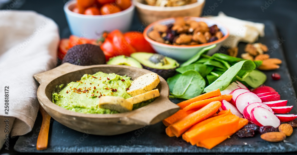 Healthy food selection with guacamole , raw veggies, green leaves spinach, herbs and ingredients, mix of nuts, clean eating, healthy vegan food