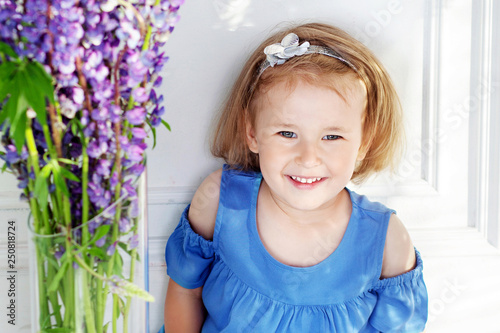 Beautiful little girl sits among violet flowers. A flower decor in an interior