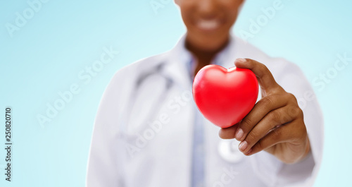 Fototapeta Naklejka Na Ścianę i Meble -  health, medicine and charity concept - close up of african american female doctor hand holding red heart over blue background