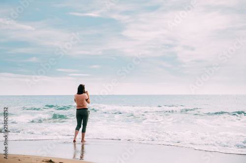 Young Caucasian Woman Standing On Summer Sea Ocean Beach And Taking Photos On Smartphone.