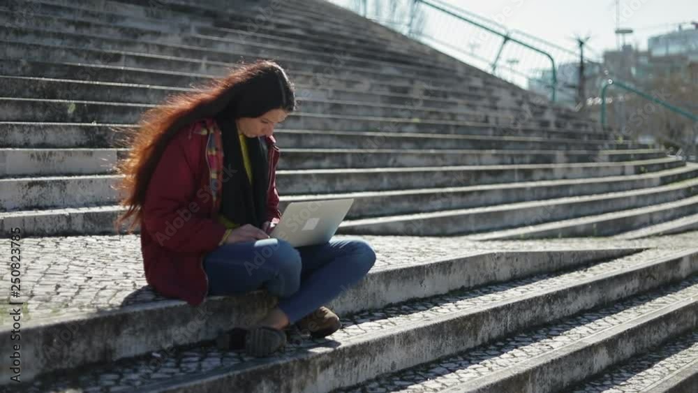 Thoughtful beautiful woman sitting on stairs with laptop on knees. Tired female student using laptop while sitting outdoor during sunny day. Businesswoman closing laptop.Overwork concept Thoughtful beautiful woman sitting on stairs with laptop on knees. Tired female student using laptop while sitting outdoor during sunny day. Businesswoman closing laptop.Overwork concept
