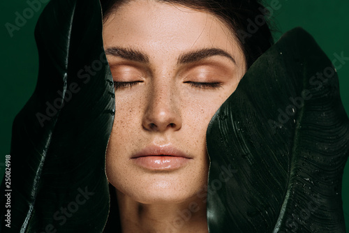 Portrait of beautiful girl with closed eyes posing with green leaves isolated on green