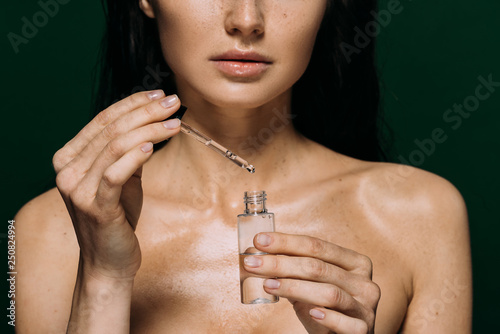 cropped view of naked woman holding bottle with serum isolated on green