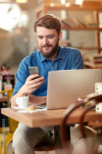 Young man looking at cell phone and work indoor